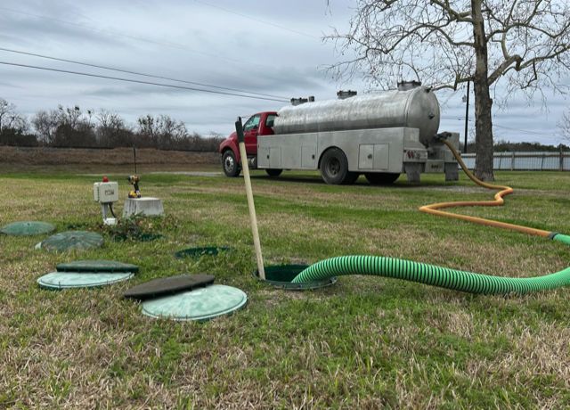 An aerobic septic system with five lids opened in a lawn, suction hoses running to the red OnePump vacuum truck
