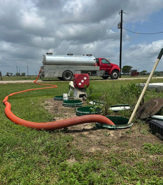 Orange suction hose running from an opened aerobic septic system across a lawn to the red OnePump vacuum truck parked on the drive