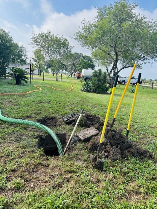 A OnePump suction hose running into an opened septic tank in a yard, with the vacuum truck parked at the roadside