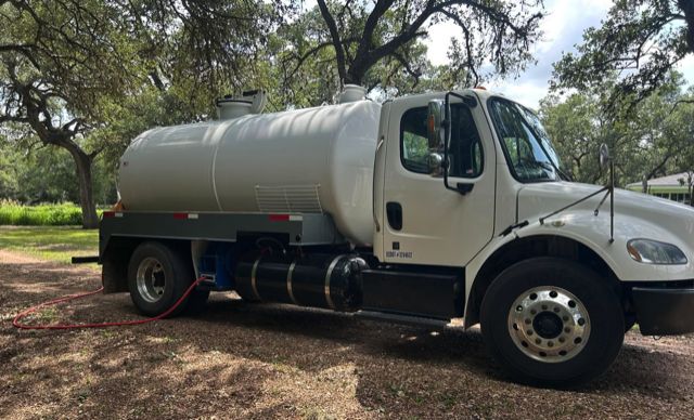 The white OnePump vacuum truck parked under live oaks on a gravel drive at a rural property