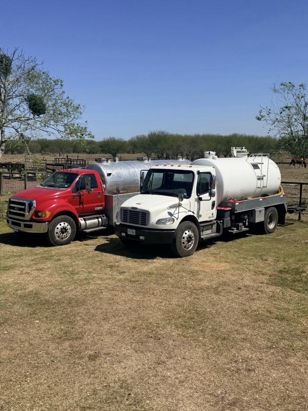 Both OnePump vacuum trucks parked on pasture under a clear Texas sky